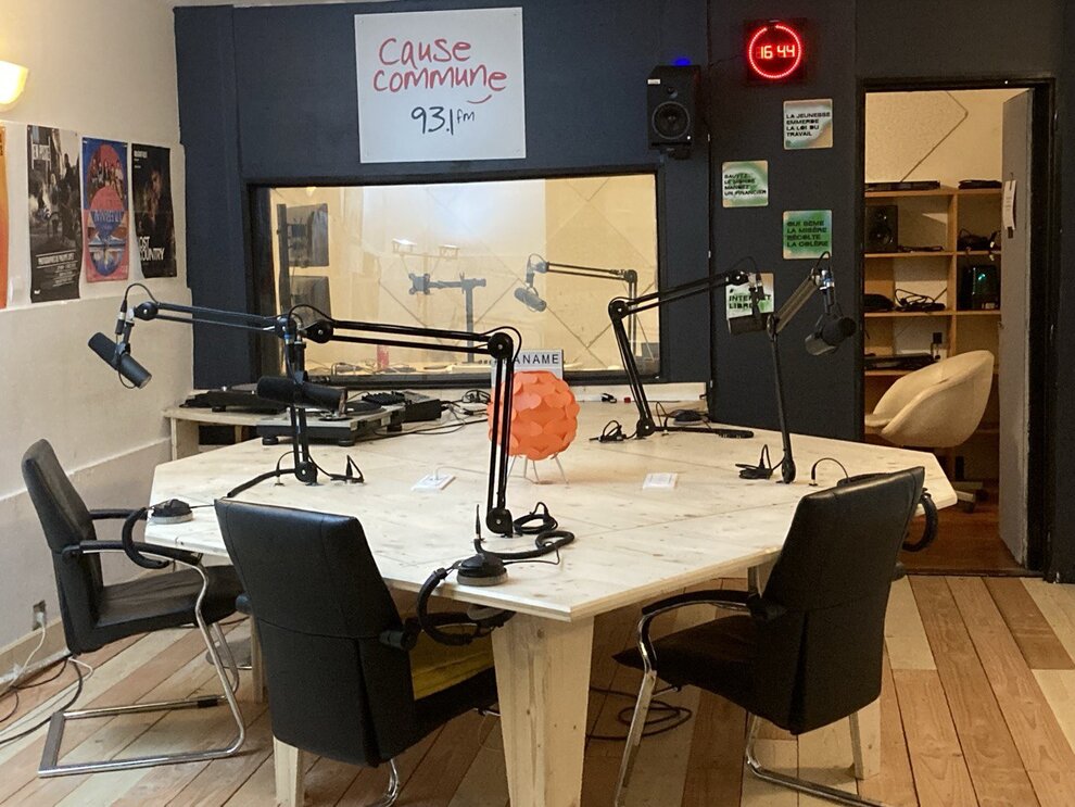 photo du plateau du studio. 4 chaises autour d'une table et autant de micro. La régie est visible est arrière plan derrière une vitre